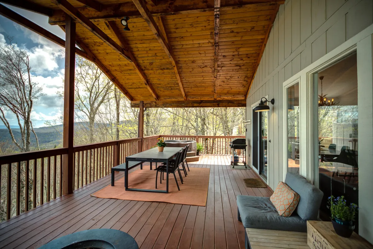 The image features a spacious wooden deck with a long dining table, ample seating, and panoramic views of the surrounding natural landscape. The setup invites communal outdoor meals, barbecues, and relaxation while taking in the scenery.