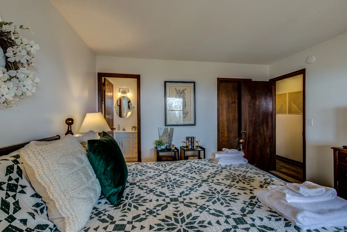 A cozy bedroom scene with a patterned quilt, decorative pillows, wall art, and a table with plants and books. The atmosphere is perfect for unwinding after a fun-filled day with family, reading stories, or simply relaxing together.