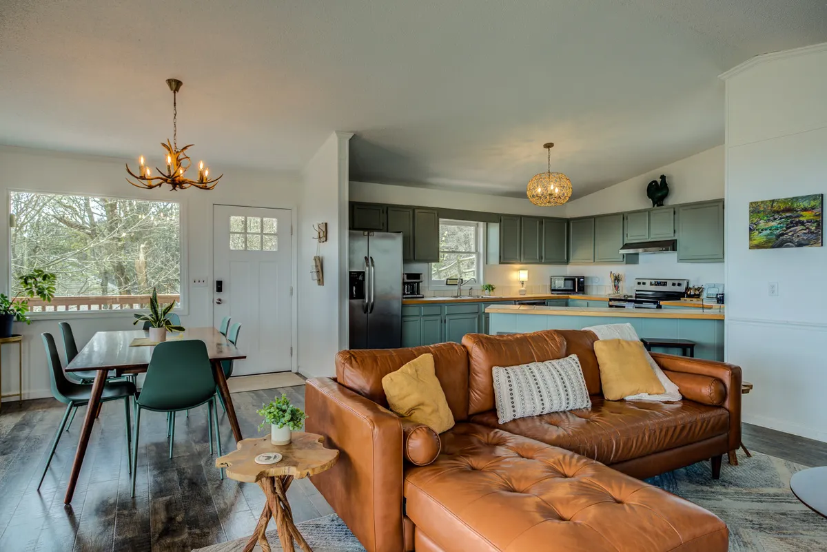 A vibrant, open-concept space featuring a brown leather sofa, a dining table with green chairs, and a modern kitchen area with stylish lighting. The arrangement is ideal for family meals, brunches, and socializing after a day of exploring local attractions.