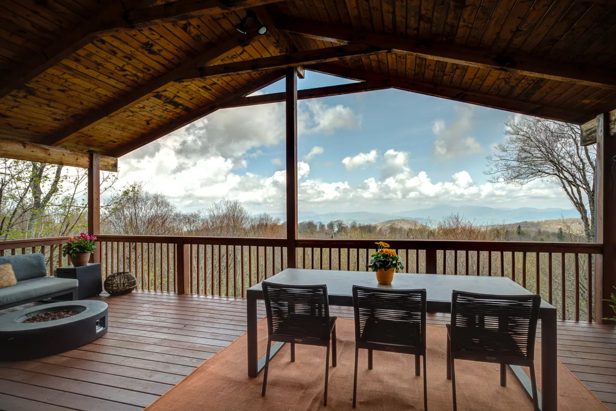 This exterior image features an outdoor dining table and a comfortable seating area set on a scenic deck. The panoramic view reveals rolling mountains and lush greenery, inviting guests to relax and enjoy the outdoors. The arrangement suggests an ideal spot for unwinding after an active day on the trails, as well as for social gatherings.